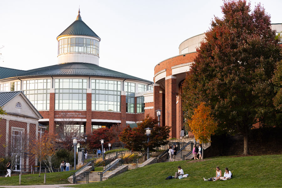 Campus library with domed rotunda, brick facade, autumn trees, walkways, and students sitting and walking.