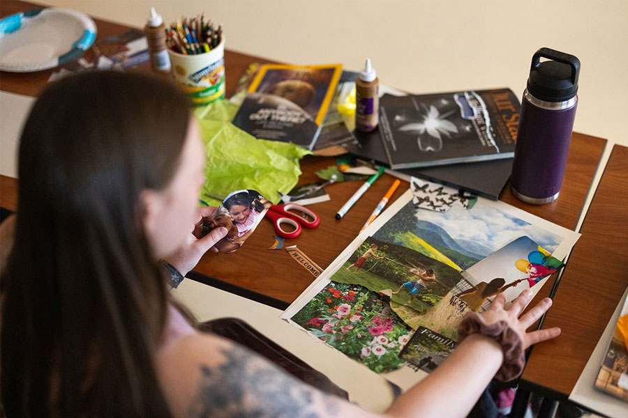 Person creating a collage at a table covered with craft supplies and magazines.