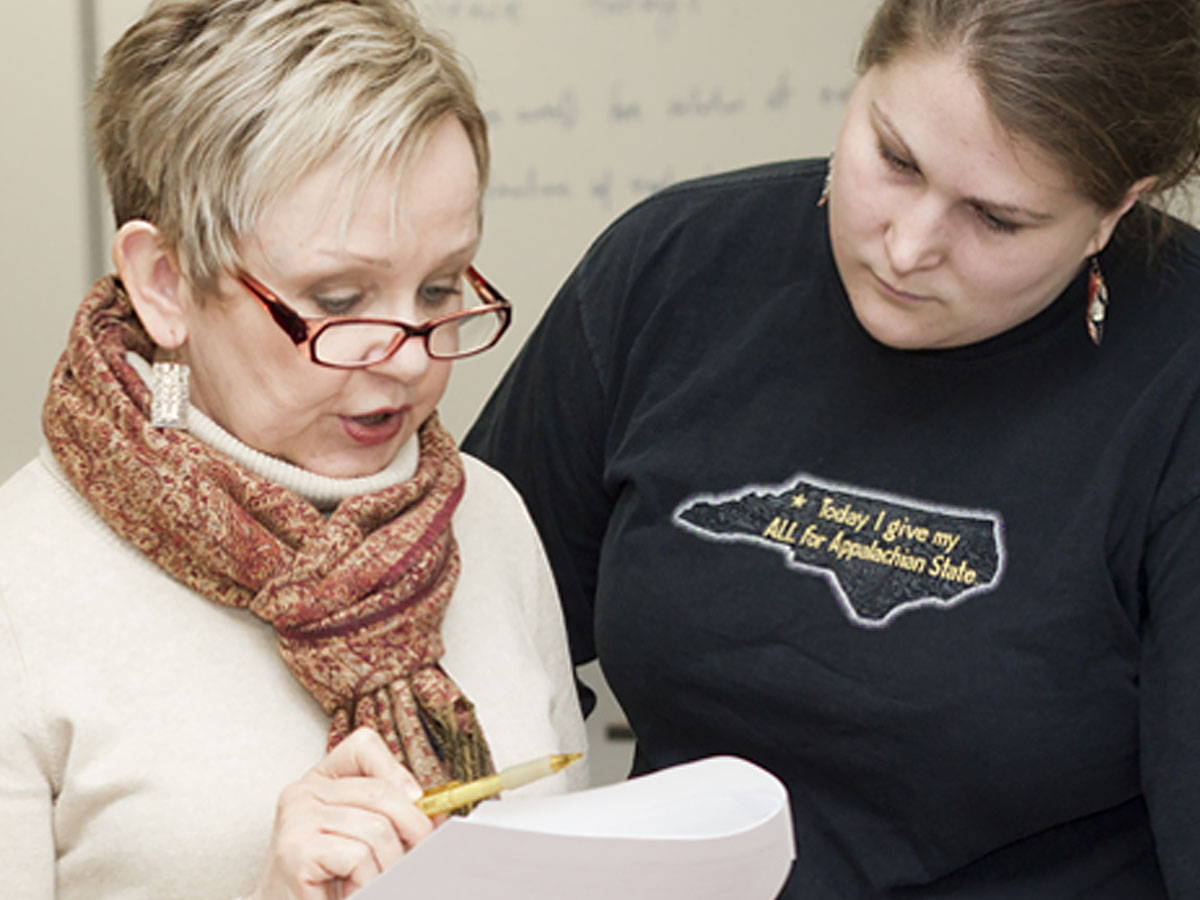 Two people standing close together reviewing a sheet of paper, one holding a pencil and the other wearing a shirt with a state outline graphic.