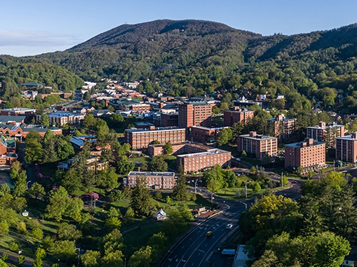 Aerial view of a campus with multiple brick buildings surrounded by trees and mountains.