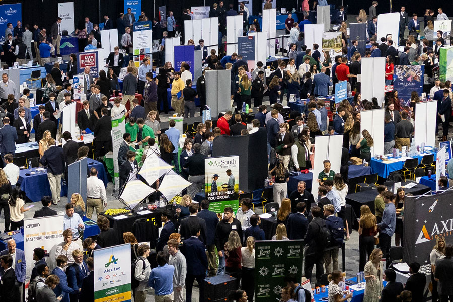 Large career fair with rows of employer booths and students networking inside an arena.