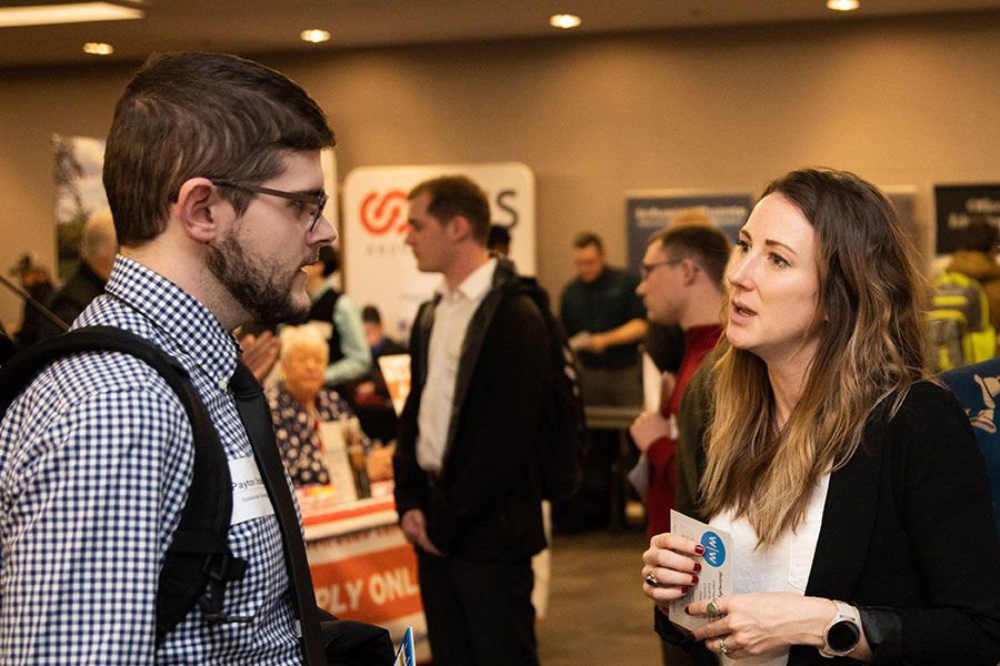 Students and professionals are interacting with employer booths to discuss opportunities. 