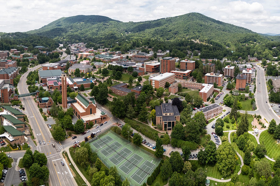 Aerial view of a university campus with academic buildings, green spaces, and surrounding hills.