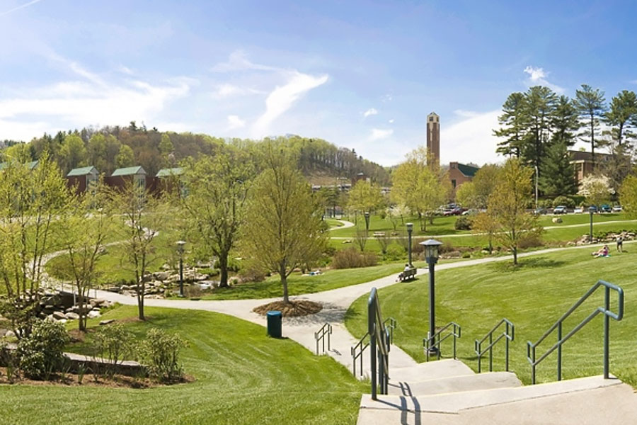 Green campus landscape with walkways, trees, and academic buildings in the distance.