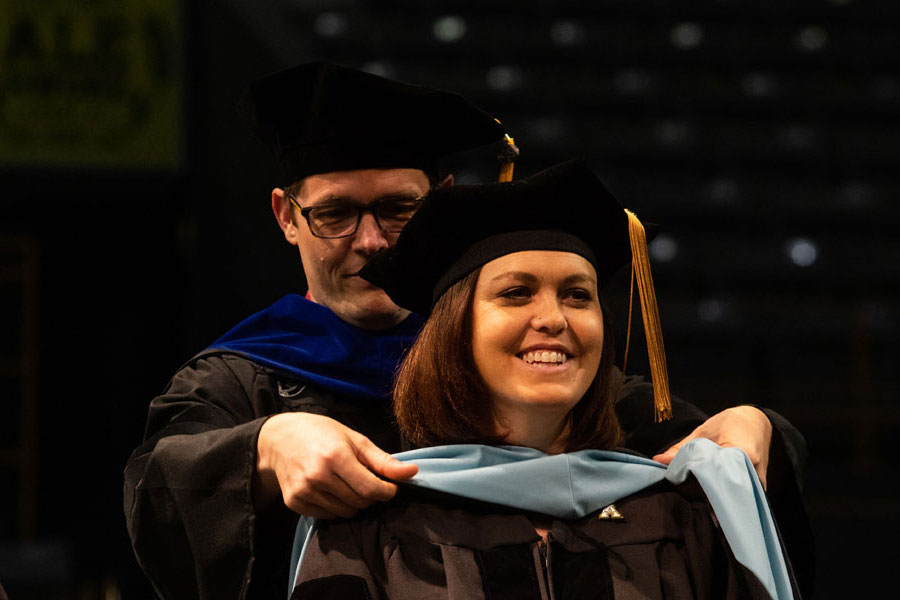 Image captures a doctoral hooding ceremony, a significant milestone where a graduate is recognized for completing their doctoral degree. 