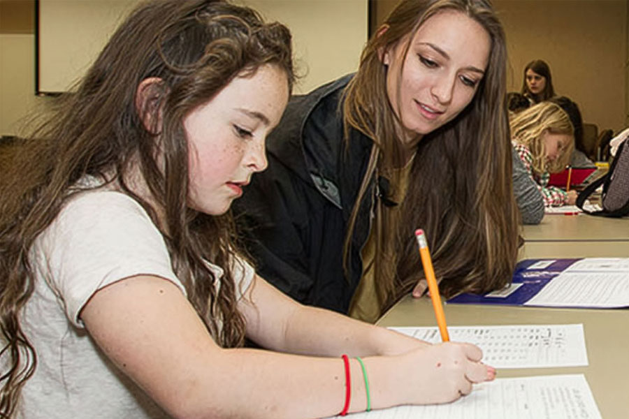 An instructor assisting a student writing on a worksheet at a classroom table.