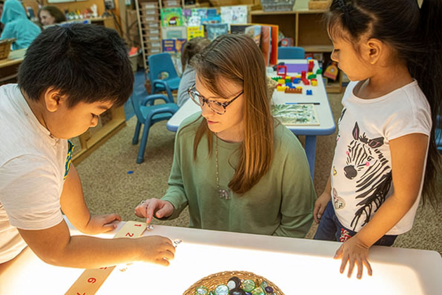 A classroom setting where a teacher and children are engaged in early learning activities at a light table.