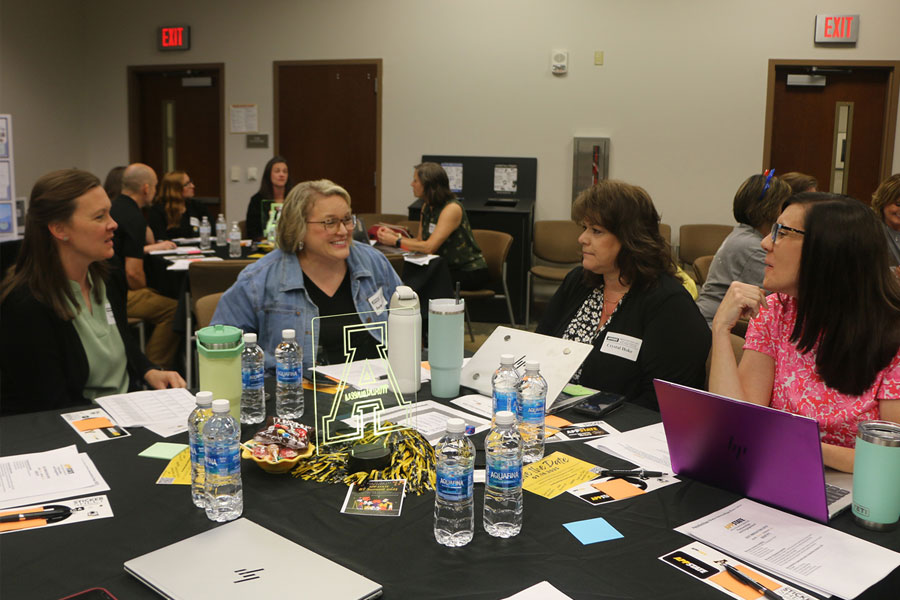 Community partners seated at tables during a collaborative meeting with materials and laptops.