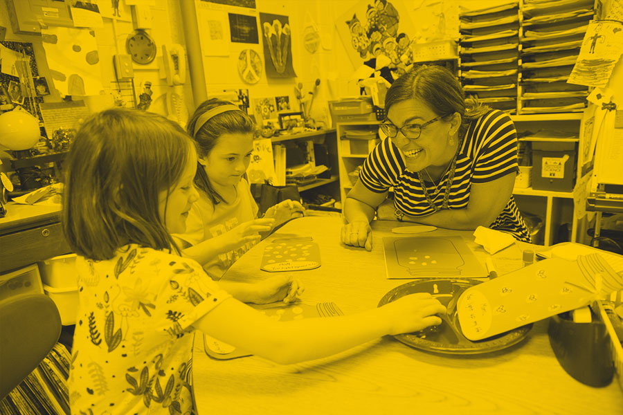 Instructor and children working together at a table with hands-on learning materials in a classroom.