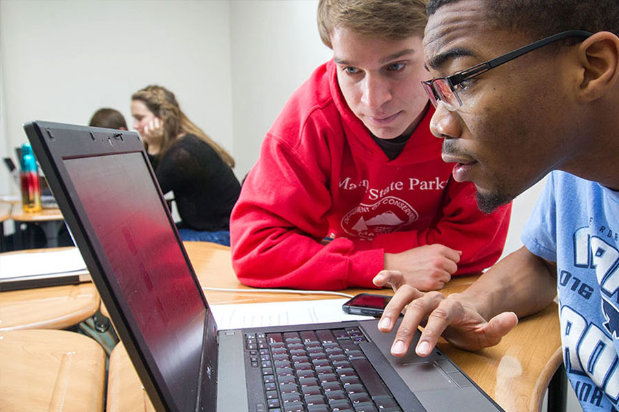One student is assisting another with coursework on a laptop computer.