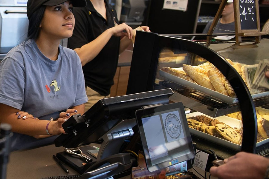 Student employee working at a campus café counter with pastries and a point-of-sale system.