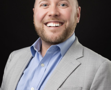 Professional photo of man in suit jacket and shirt, smiling. 