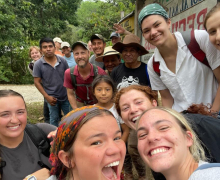Group of people outdoors on a hiking or study-abroad trip, standing near a sign with trees in the background.