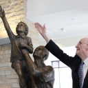 Irwin “Ike” Belk mimics the gesture of the bronze boy in “Just Reach a Little Higher,” a sculpture he commissioned for the Reich College of Education in 2012.