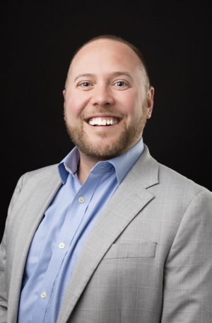 Professional photo of man in suit jacket and shirt, smiling. 