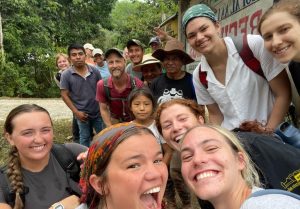 Group of people outdoors on a hiking or study-abroad trip, standing near a sign with trees in the background.