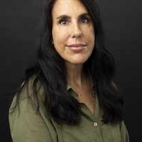 Professional headshot of a person with long dark hair wearing a green button-up shirt against a dark background.