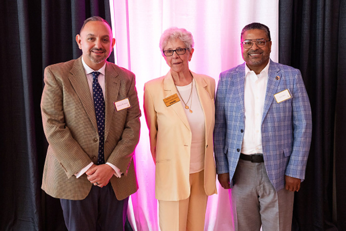 Three people pose with name badges before pink-lit drapery.