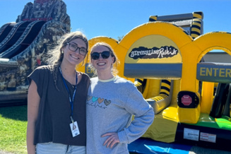 Two people volunteering in front of jump house slides. 