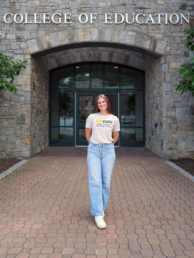 Kat Plutzer in an App State North Carolina Teaching Fellows t-shirt in front of the RCOE building.