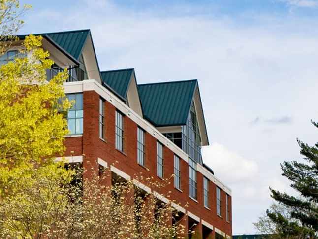 Reich College of Education building framed by spring trees beneath a bright blue sky with scattered clouds.