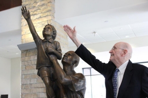Irwin “Ike” Belk mimics the gesture of the bronze boy in “Just Reach a Little Higher,” a sculpture he commissioned for the Reich College of Education in 2012.